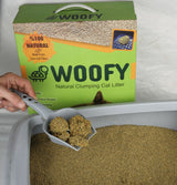 Wir sehen die 10-Liter-Produktbox „Woofy natürlich klumpende Katzenstreu“ in Grün und verklumpten Sand